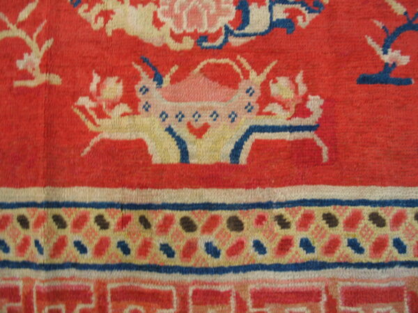 Red rug detail featuring a stylized floral basket design and geometric borders in blue, cream, and pink.