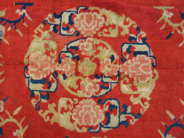 Close-up of a red rug featuring a circular floral medallion pattern in pink, yellow, cream, and blue.