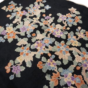 Close view of a round black rug with a multicolor floral branch design in peach, blue, and purple.