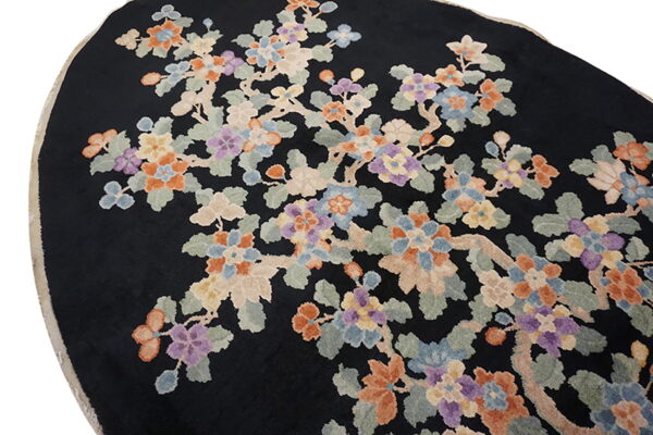 Close view of a round black rug with a multicolor floral branch design in peach, blue, and purple.
