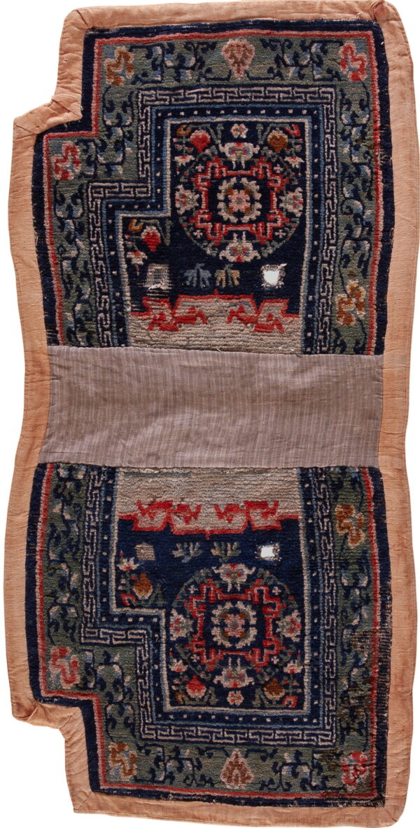 A vertically oriented, patterned textile fragment features navy, green, and red designs with a wide tan fabric border.