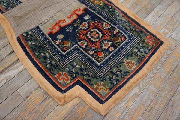 Detailed blue, green, and red patterned rug section with a tan border sits on weathered wood flooring.