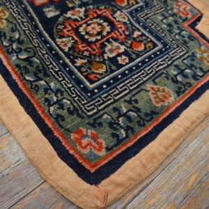 Ornate navy, green, and red rug corner with a wide tan border lying on weathered wood flooring.
