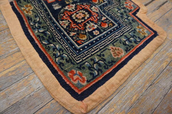 Ornate navy, green, and red rug corner with a wide tan border lying on weathered wood flooring.