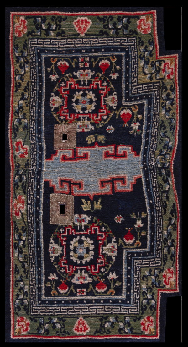 Navy blue rug featuring complex red and light blue patterns, a green border, and two stitched patches with holes.