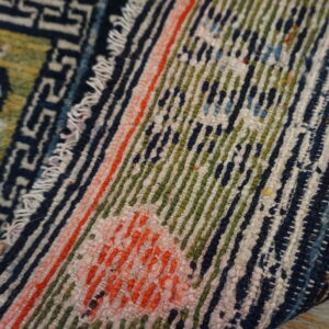Textured rug detail featuring geometric dark blue patterns alongside vivid green and coral striped sections.