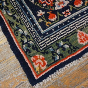 Navy blue, green, and coral floral rug with geometric borders lies on weathered hardwood floor.