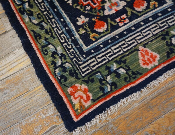 Navy blue, green, and coral floral rug with geometric borders lies on weathered hardwood floor.