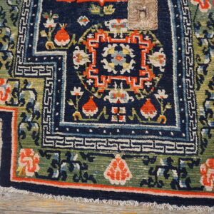 Textured navy blue rug displaying orange and green stylized floral and geometric borders on light wood floor.