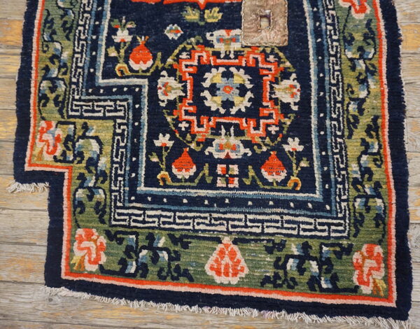 Textured navy blue rug displaying orange and green stylized floral and geometric borders on light wood floor.