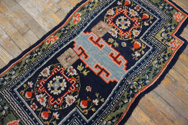 Dark blue rug with light blue geometric pattern, multicolored border, and two square patches on wood flooring.