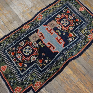 Navy, green, and red patterned rug with a light blue stepped center lies on weathered wooden planks.