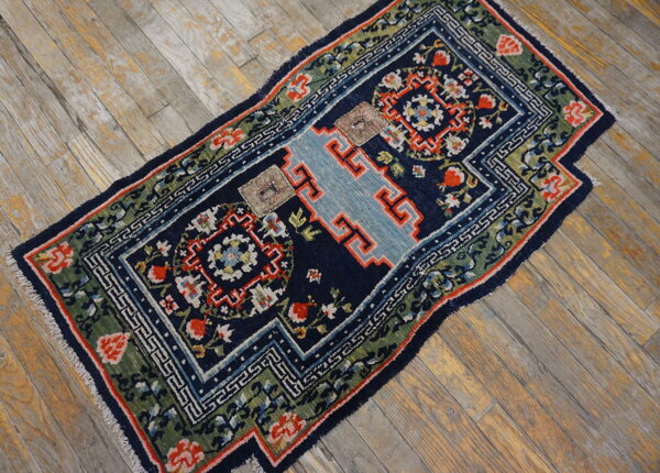 Navy, green, and red patterned rug with a light blue stepped center lies on weathered wooden planks.