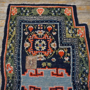 A multicolored rug featuring navy, teal, red, and green designs with a patch lies on distressed light wooden flooring.