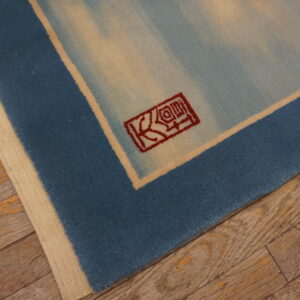 Short-pile blue and cream rug corner showing a red symbol against distressed wide plank wood flooring.
