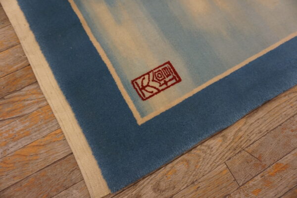 Short-pile blue and cream rug corner showing a red symbol against distressed wide plank wood flooring.