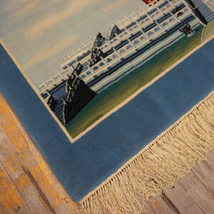 Detail of a low-pile blue pictorial rug with fringe on distressed wood plank flooring.