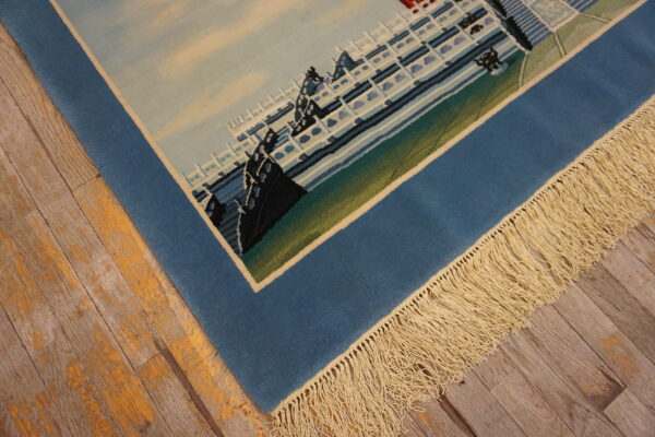 Detail of a low-pile blue pictorial rug with fringe on distressed wood plank flooring.