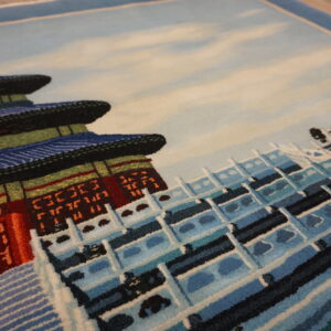 Angled view of a low-pile rug featuring a pictorial design of blue, red, and white tiered architecture.