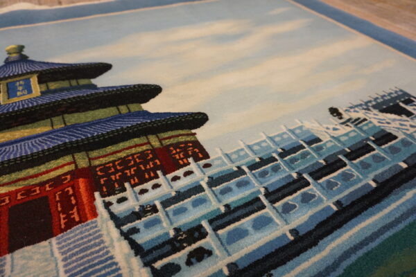 Angled view of a low-pile rug featuring a pictorial design of blue, red, and white tiered architecture.