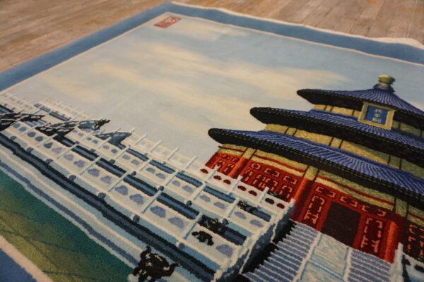 Close-up of a low-pile rug displaying a detailed blue and red tiered building scene on wood flooring.