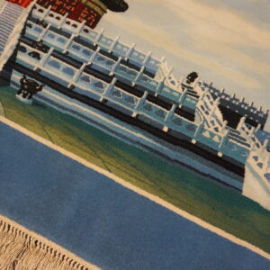 Close-up of a low-pile rug with a detailed scenic pattern in blue, white, teal, and green, bordered by fringe.