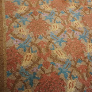 Close-up of a rug with a repeating floral pattern in rust, teal, yellow, and tan colors.