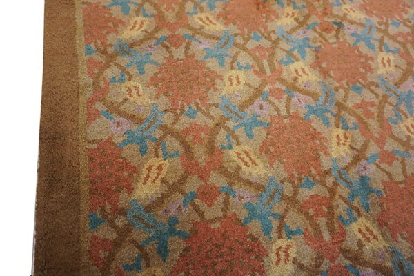 Close-up of a rug with a repeating floral pattern in rust, teal, yellow, and tan colors.