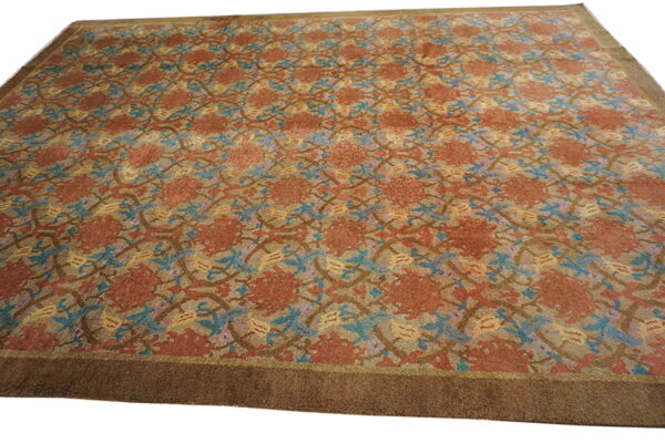 Low-pile rug with a repeating floral pattern in rust, teal, and gold, framed by a wide dark brown border.