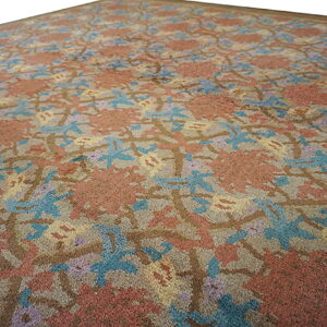 Angled view of a low pile rug featuring an abstract floral pattern in rust, blue, purple, and brown.