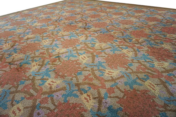 Angled view of a low pile rug featuring an abstract floral pattern in rust, blue, purple, and brown.