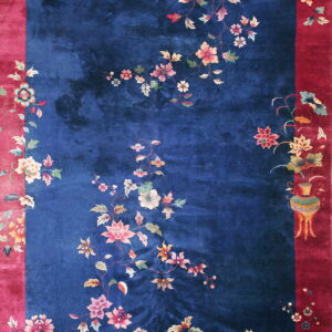 Deep blue rug with a wide crimson border detailed with colorful, ornate flowers and vines.