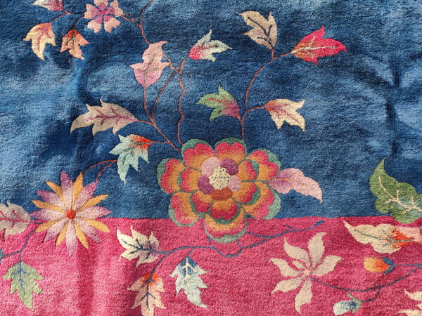 Plush rug texture with large orange, pink, and green flowers contrasting with blue and magenta fields.