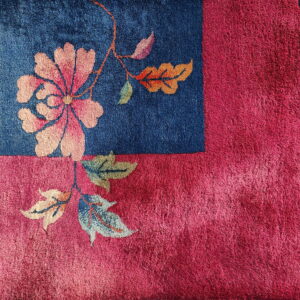 High-pile rug corner showing pink floral motif on a blue field surrounded by a magenta border.