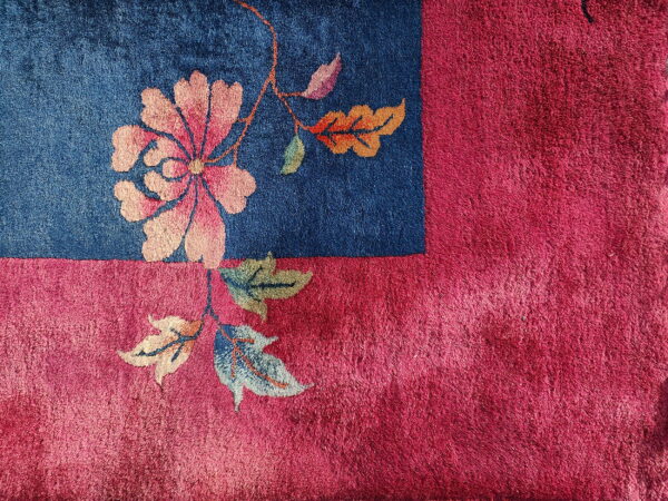 High-pile rug corner showing pink floral motif on a blue field surrounded by a magenta border.
