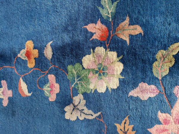 Deep blue rug texture showing large stylized floral motifs in pink, cream, and green.