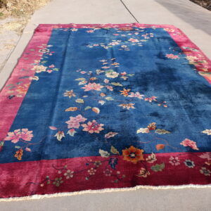 Deep blue rug featuring scattered colorful floral vines and a bright pink patterned border on gray pavement.