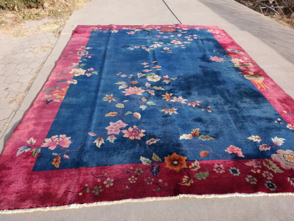 Deep blue rug featuring scattered colorful floral vines and a bright pink patterned border on gray pavement.