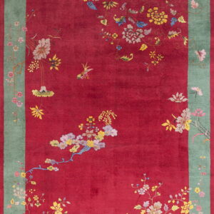 Plush red rug with scattered colorful floral and bird designs and a wide green decorative border.