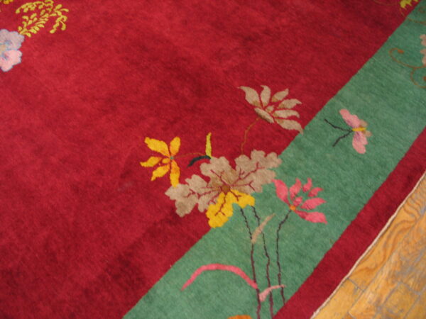 Red floral patterned rug with a diagonal green border strip rests on a polished wood floor.