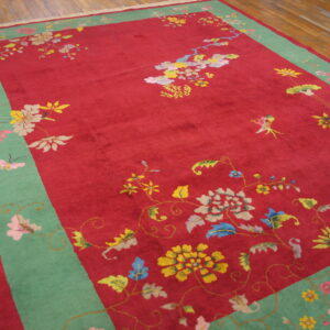 Low-pile red rug featuring colorful floral motifs, a wide mint border, and visible wood flooring.