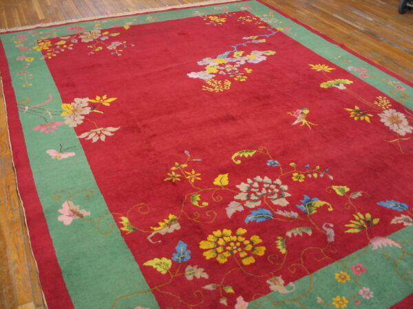 Low-pile red rug featuring colorful floral motifs, a wide mint border, and visible wood flooring.