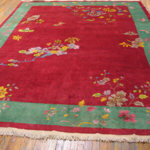 Red high-pile rug with a wide green border and multicolored floral patterns on wood plank flooring.