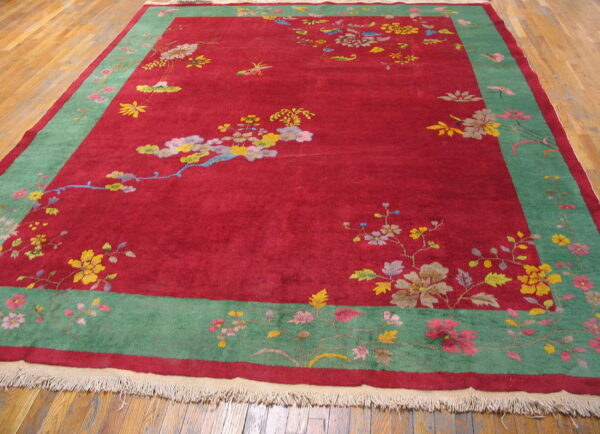 Red high-pile rug with a wide green border and multicolored floral patterns on wood plank flooring.