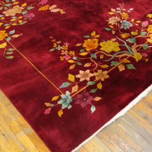 Corner view of a plush burgundy rug with multicolored floral branches on a light wood floor.