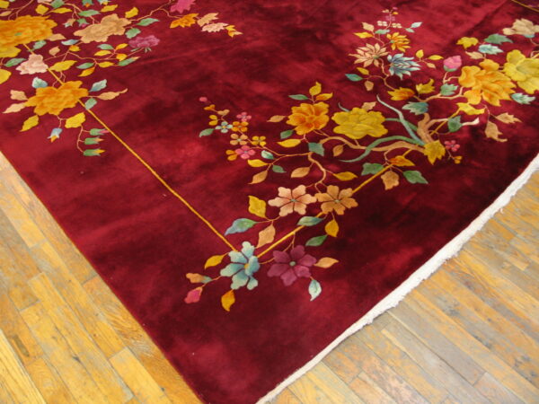 Corner view of a plush burgundy rug with multicolored floral branches on a light wood floor.