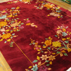 Velvety burgundy rug featuring vibrant yellow and pink floral branches framing the center, lying on wood flooring.