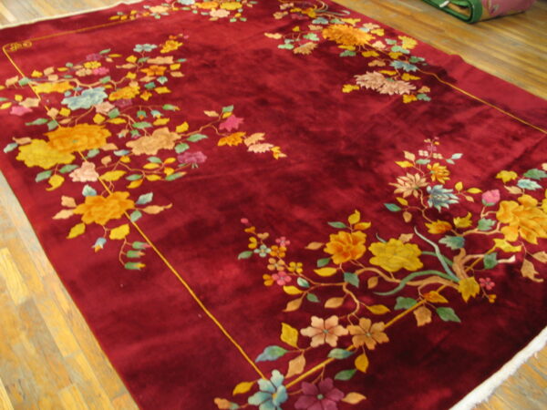 Velvety burgundy rug featuring vibrant yellow and pink floral branches framing the center, lying on wood flooring.