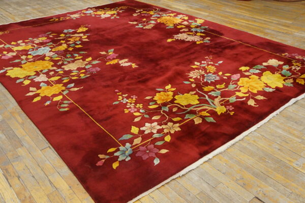 Plush red rug featuring a border of yellow, pink, and blue flowers rests on rustic wooden floorboards.