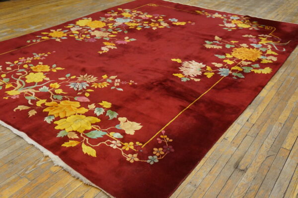 Crimson high-pile rug featuring yellow, blue, and pink floral designs on light brown wood planks.
